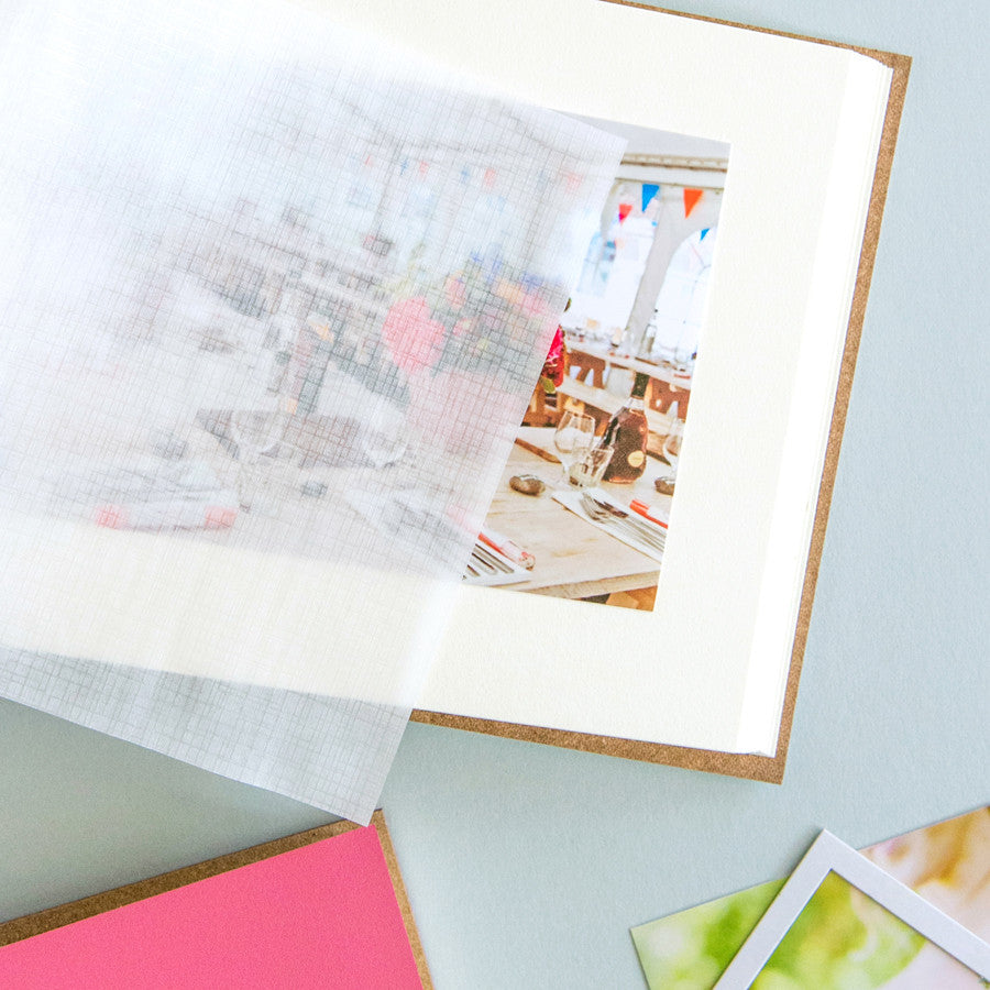 a photo album lies open on the table and you can see a photo inside of the album and the glassine page lying over the top