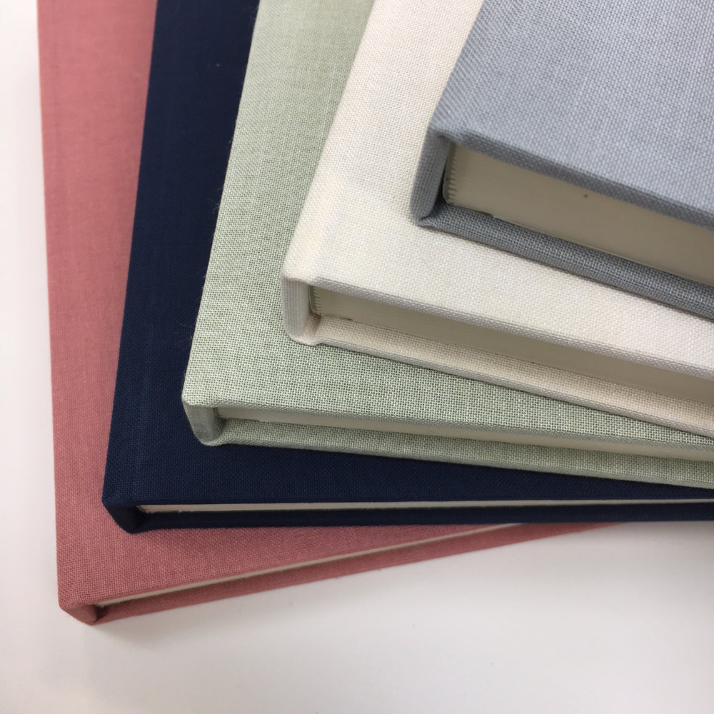 
                      
                        four linen wedding guest books are in a pile. All made by BeGolden
                      
                    