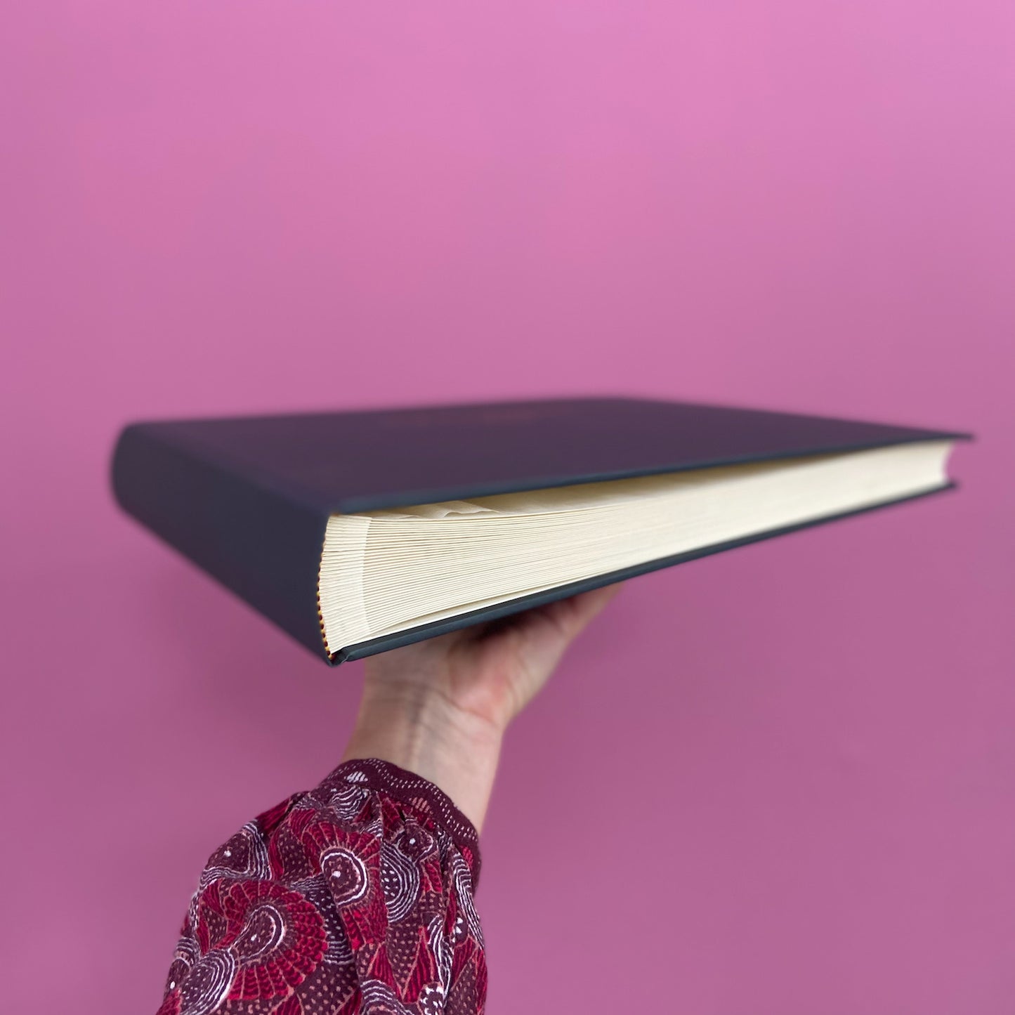 a hand holds up a large guest book so you can see it from the side. You can see the traditional binding