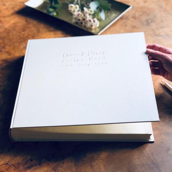 on a wooden table is a large ivory wedding album that has been personalised with wedding detals 