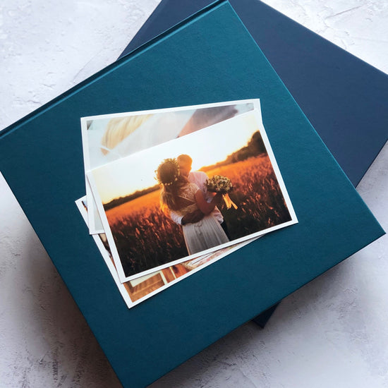 two blue personalised photo albums are on a table. On top of the photo albums are some photos of a bride and groom