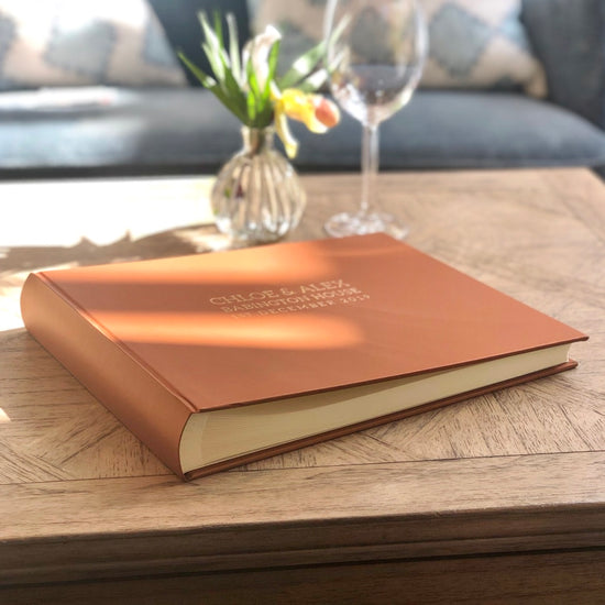 the sun shines on a brown wedding guest book that has been placed on a coffee table for people to sign
