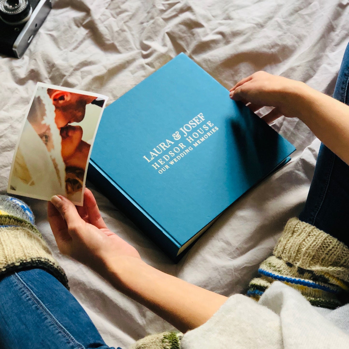 Woman sitting on a bed putting wedding photos into a beautiful blue photo album.