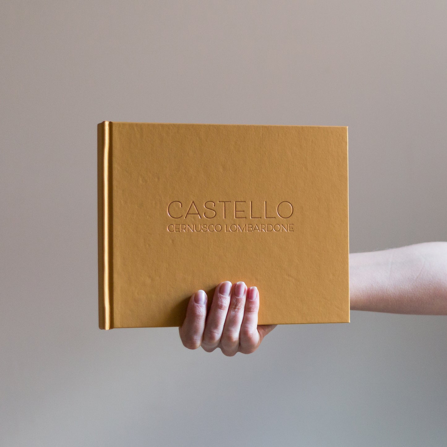 against a grey background a woman holds up a yellow guest book which has been printed with rose gold foil. 