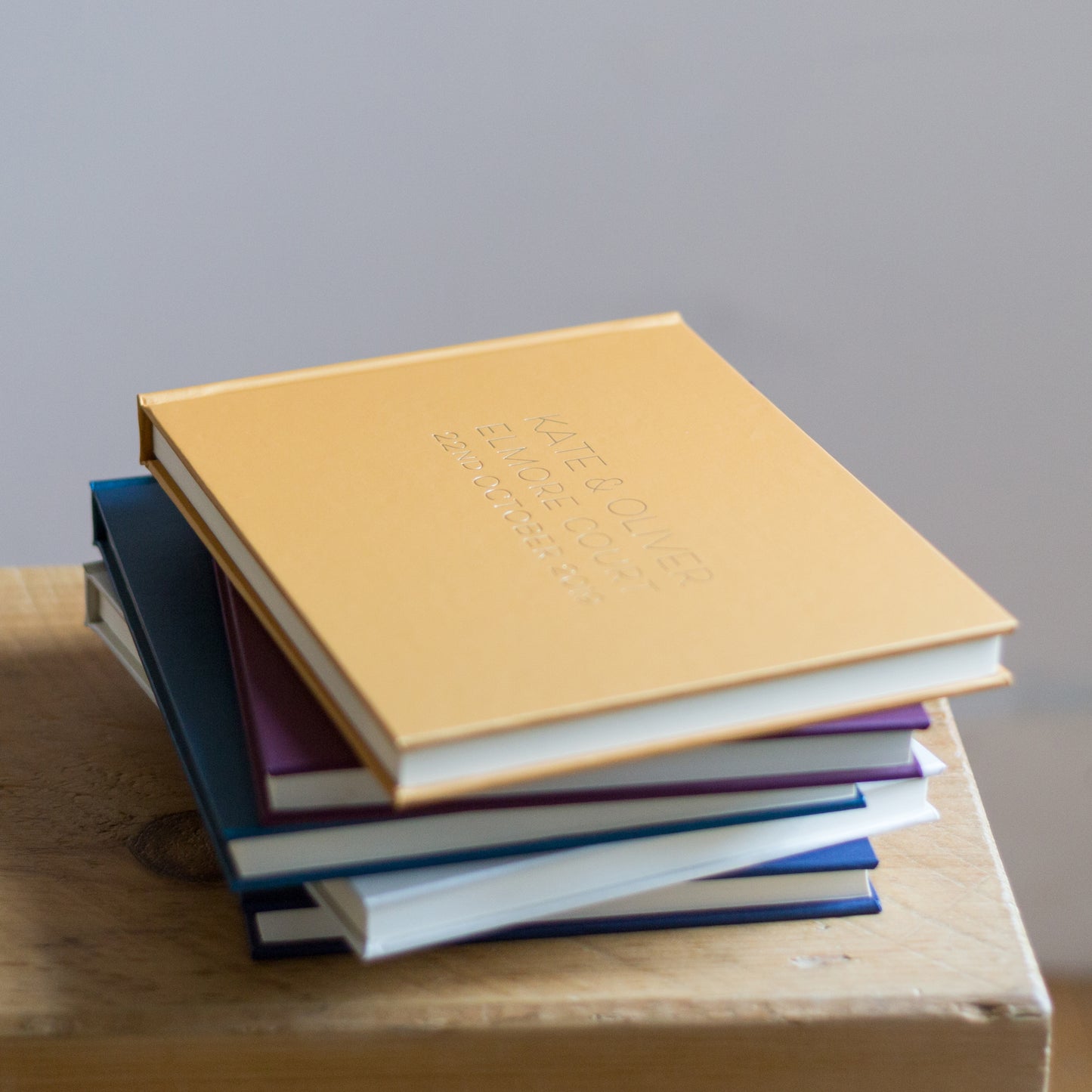 a pile of guest books are on a wooden table, a yellow one is on the top