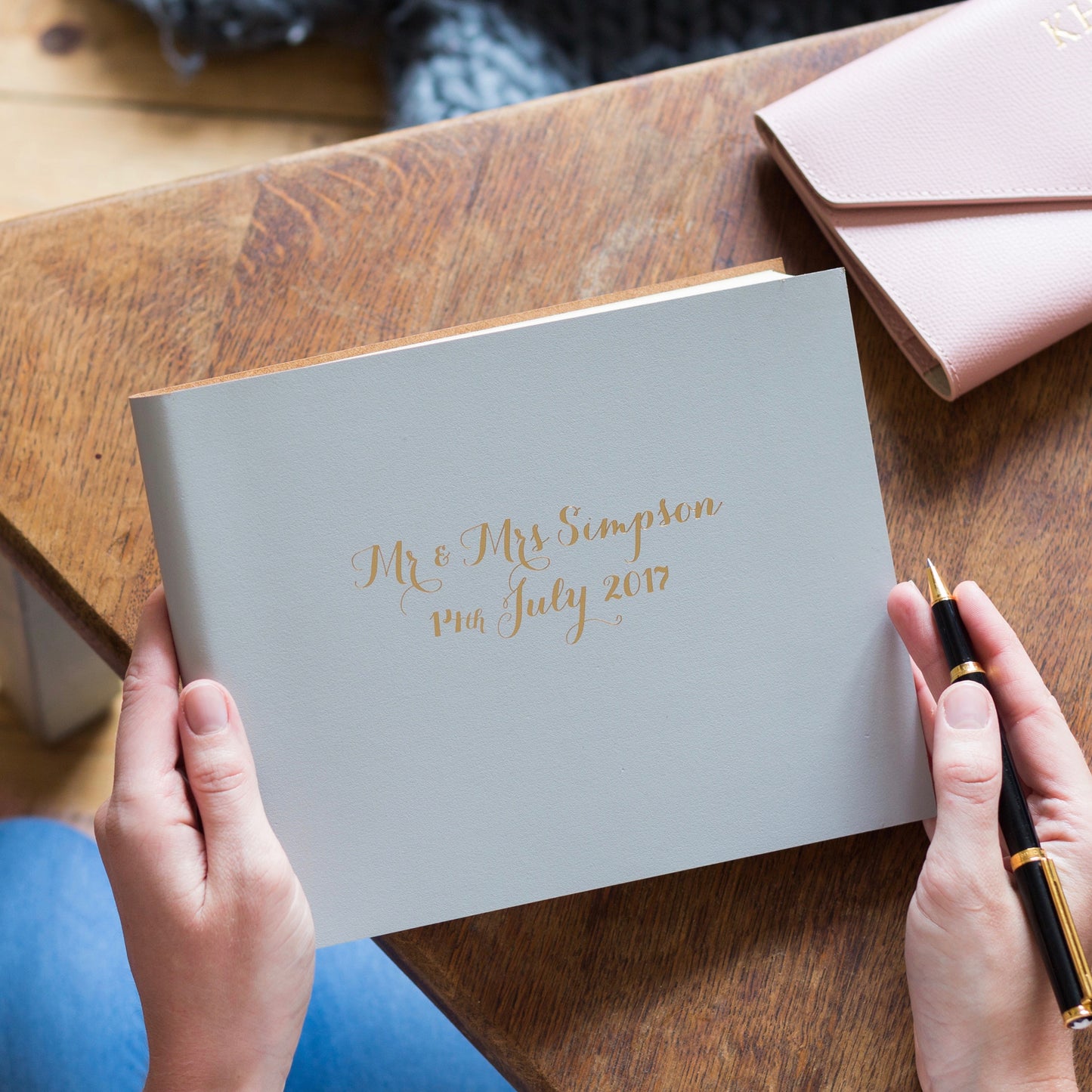 a wedding guest book is on the table and a guest is poised with a pen about to write a message in it