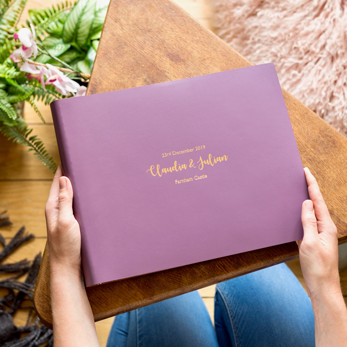 Plum coloured wedding album with gold lettering, resting on a wooden table.