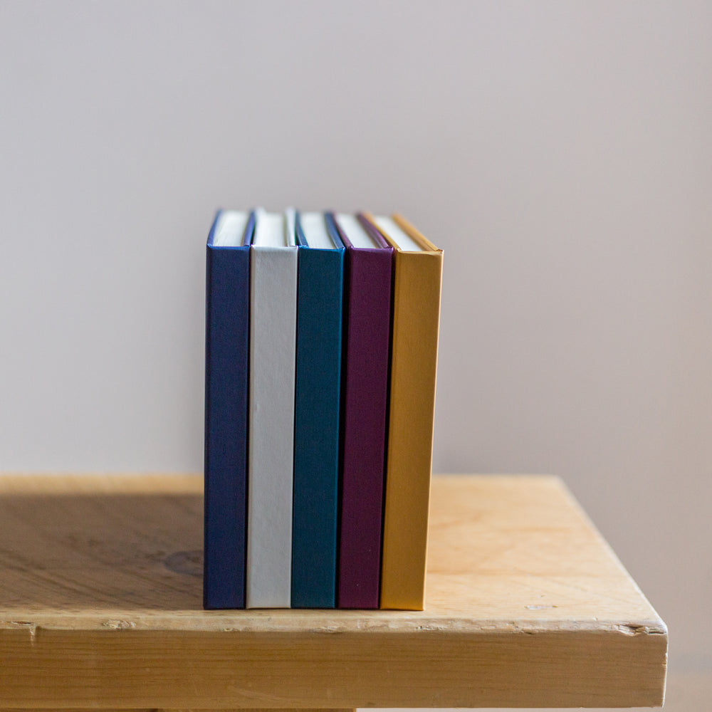 
                      
                        Five guest books are standing on the end of a wooden table. They are all different colours.
                      
                    