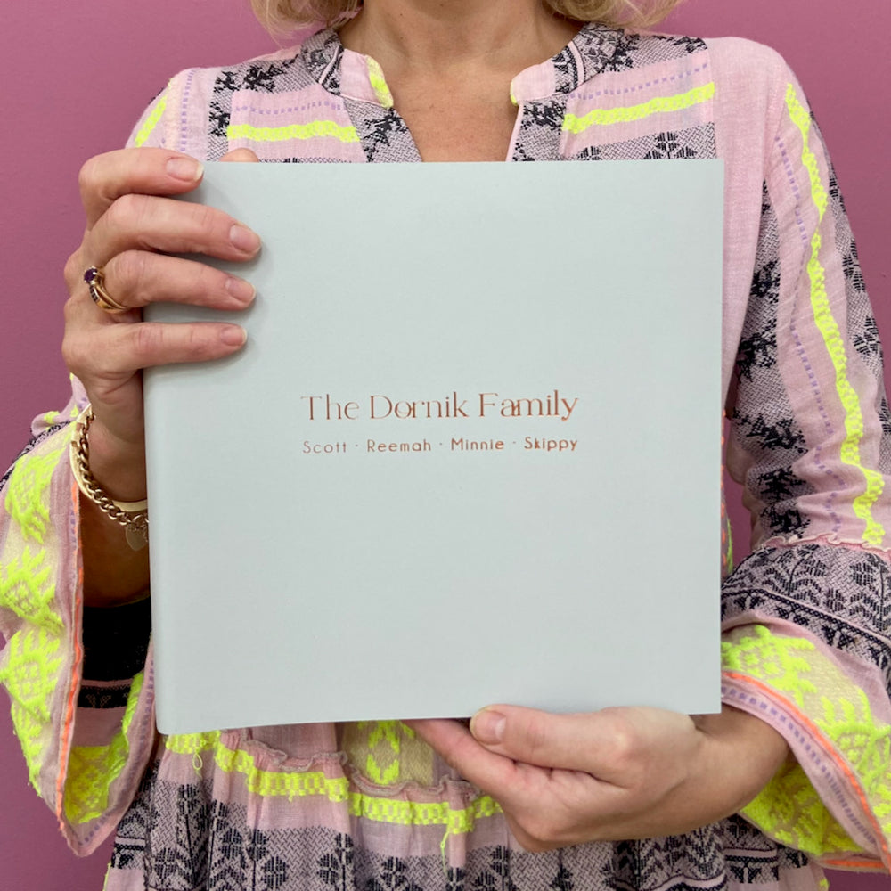 
                      
                        A woman is holding a large family photo album. In the colour ivory, this album has been personalised with their families names with gold hot foil. 
                      
                    