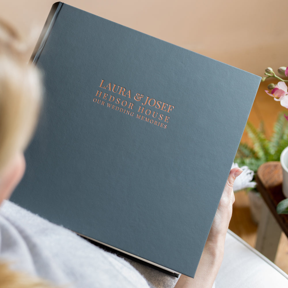 
                      
                        A woman is holding a large black photo album in her hands. You can see that it has been printed on the front with wedding details.
                      
                    