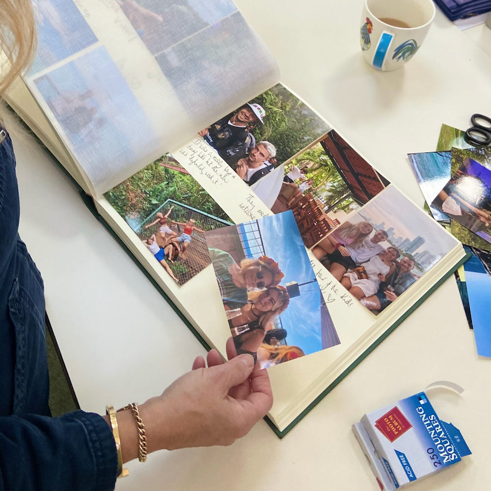 
                      
                        A large photo album is open on a coffee table. It is full of holiday photos. There is a box of mounting squares to the side of the album.
                      
                    