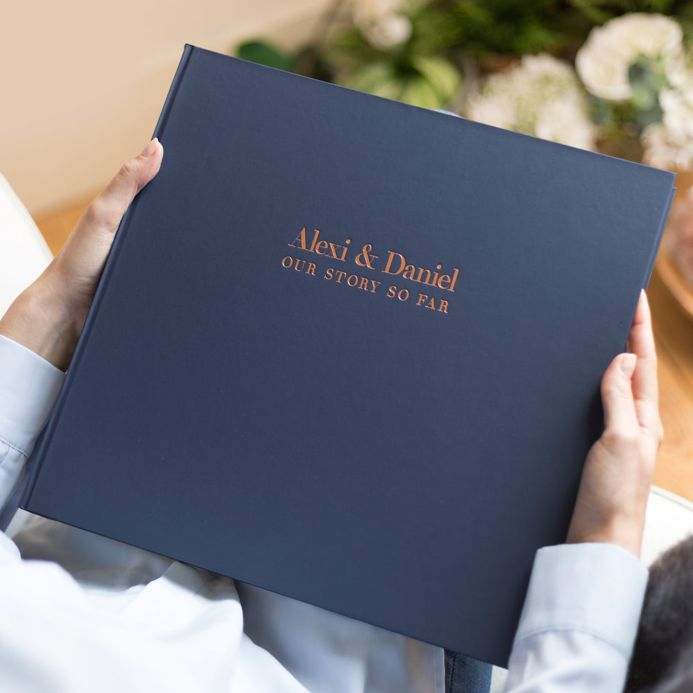 There is a man holding a large photo album. The album has been personalised with both partners names in a copper foil. 
