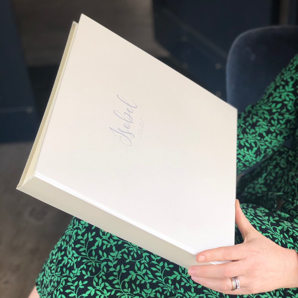 
                      
                        There is a woman holding a large white jewel album. It has been personalised with silver hot foiling on the front in the centre of the album. 
                      
                    