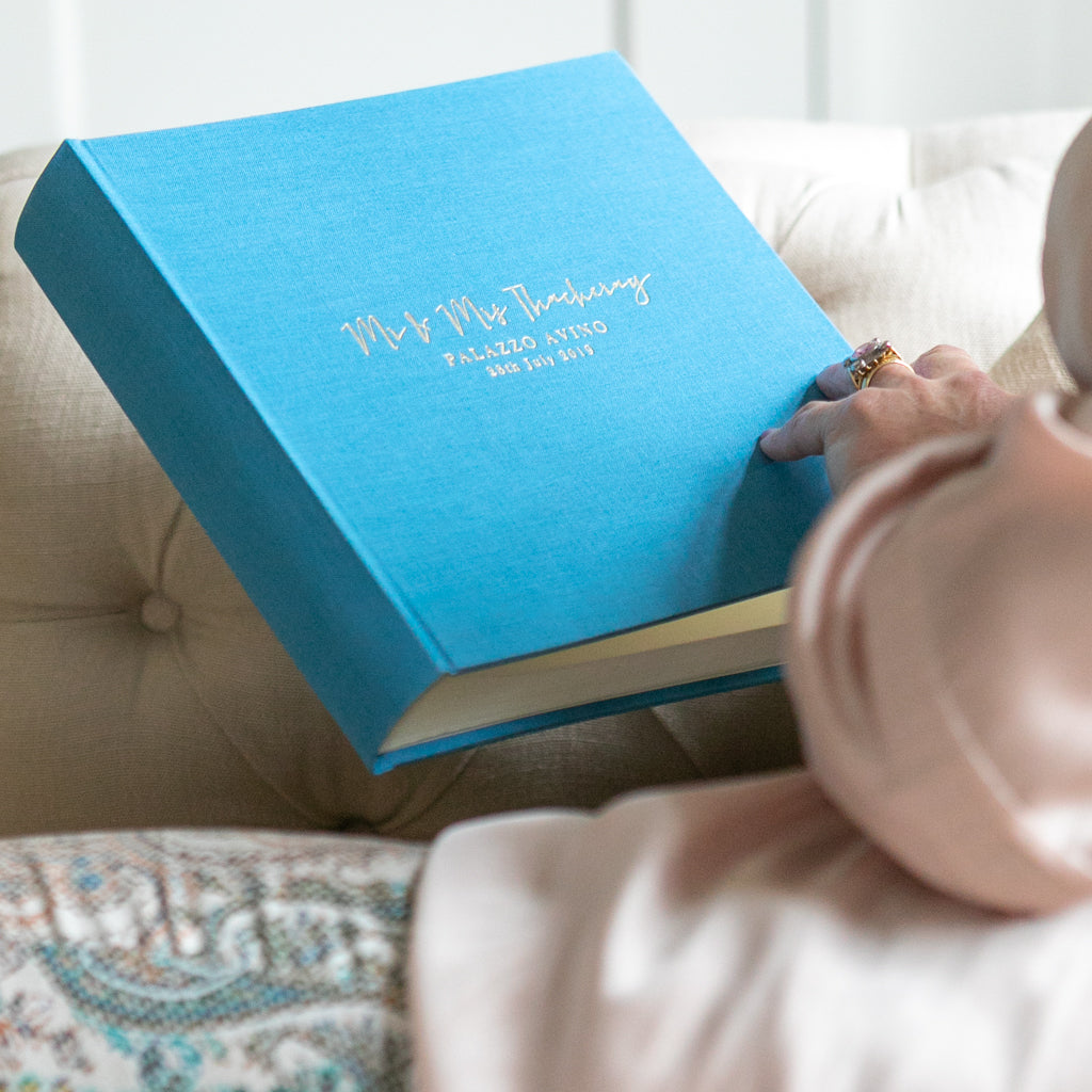 There is a woman holding a blue linen guest book. It has been personalised on the front with gold hot foil.