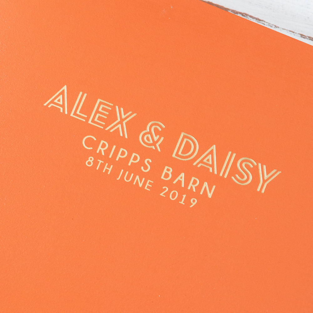 
                      
                        This is a close up shot of an orange guest book. There are personalised details on the front in gold foil.
                      
                    