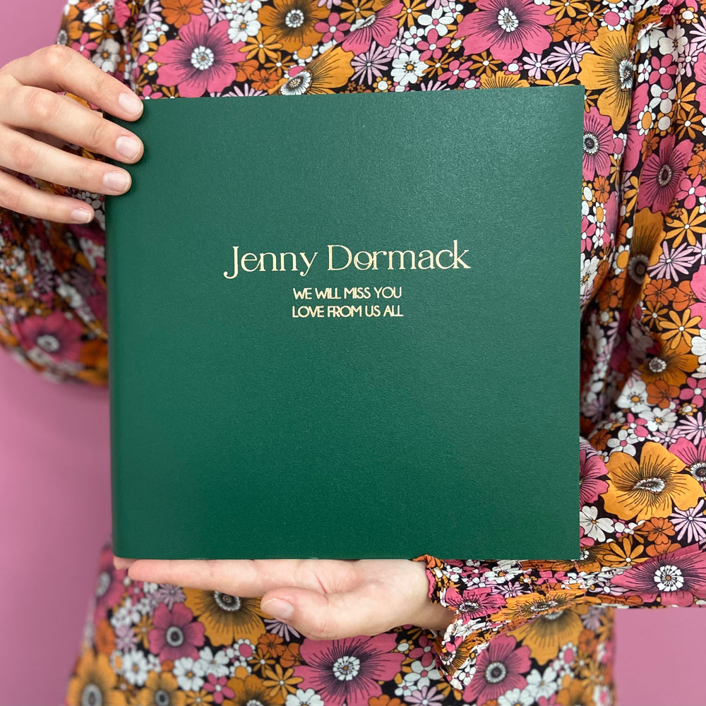 A woman in a flowery dress holds a personalised retirement book that has been personalised with details. 