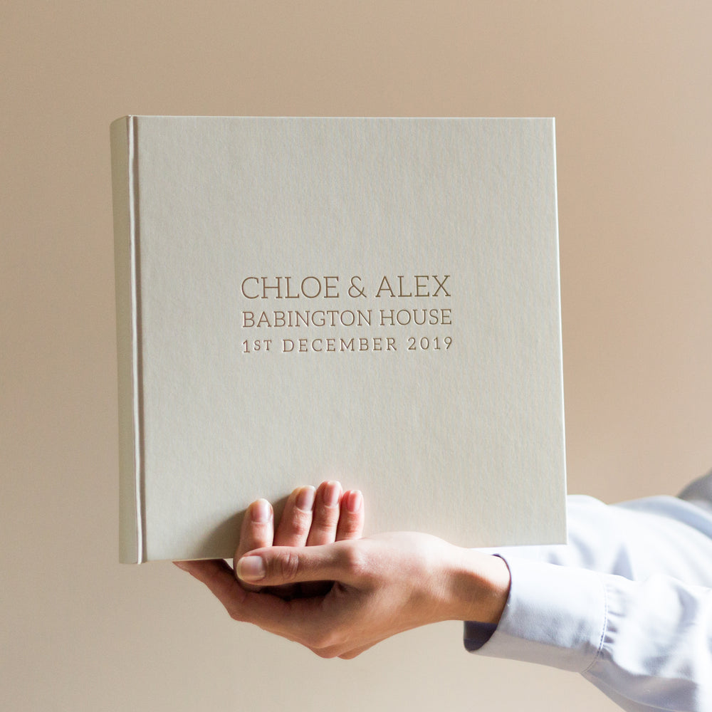 There is someone cupping their wedding album. There is hot foil personalisation on the front with their wedding details. 