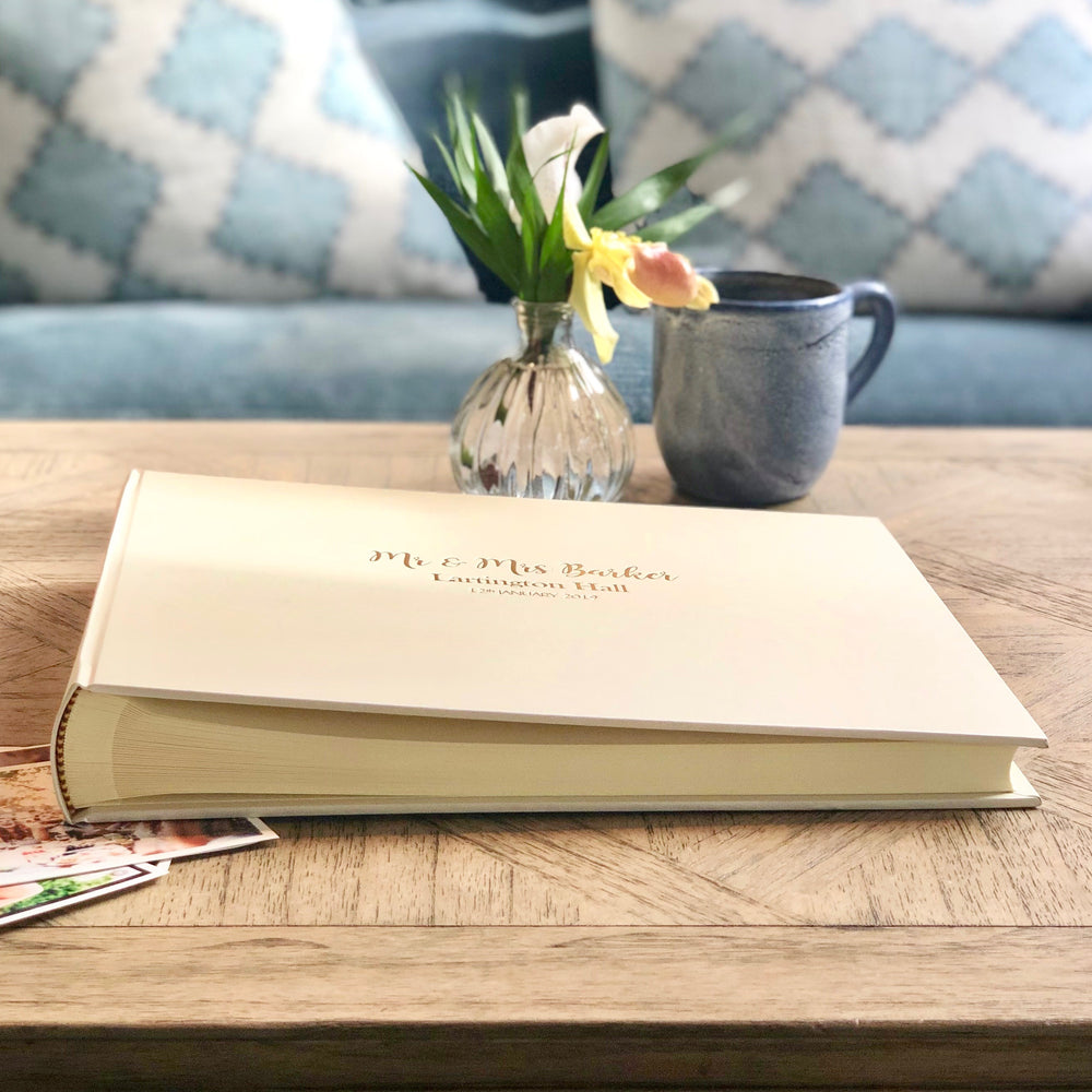 
                      
                        This is a side view of the personalised wedding guest book. It has been placed on a coffee table in front of a mug of tea and a posy of flowers. 
                      
                    