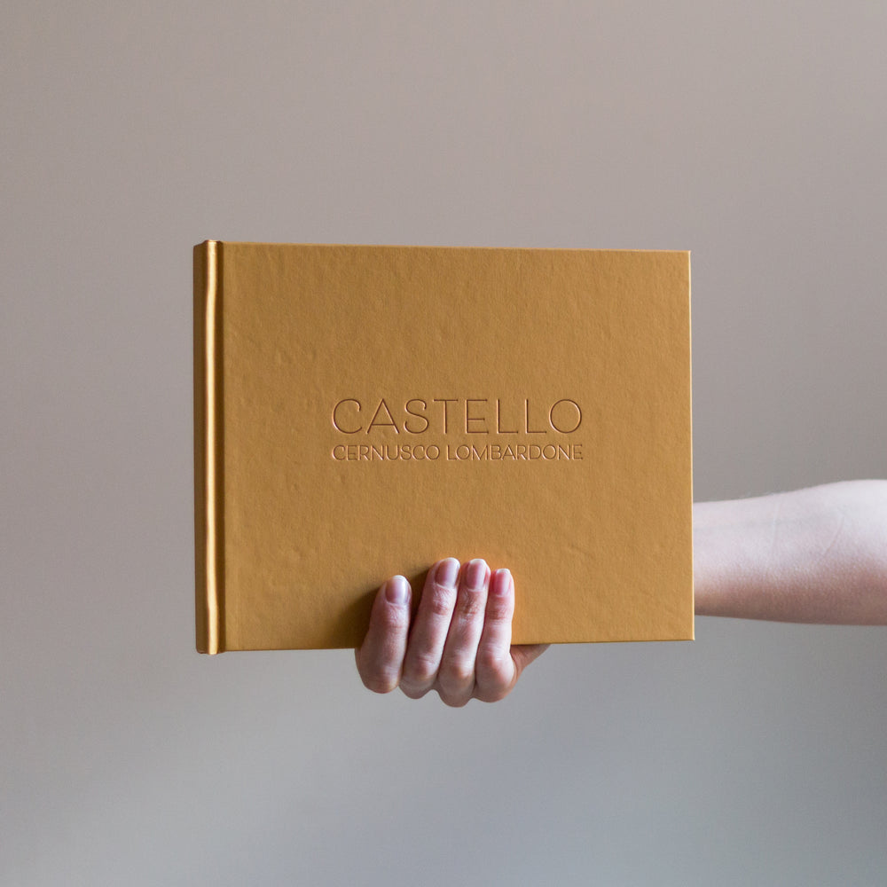 Against a grey background a woman holds up a yellow guest book which has been printed with rose gold foil. 